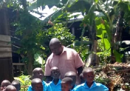 A teacher sitting with children under the trees at the centre